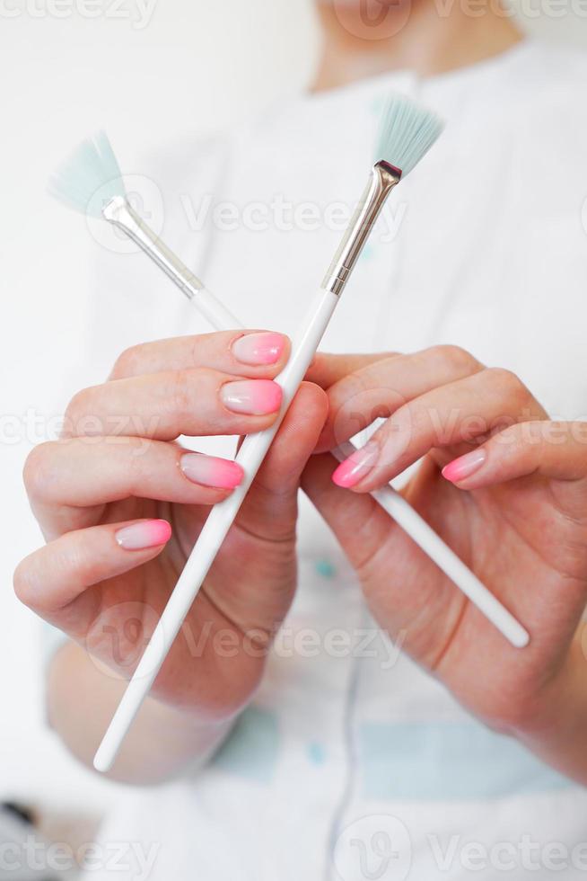 cosmetologista em equipamento médico segurando dois pincéis cosmológicos foto