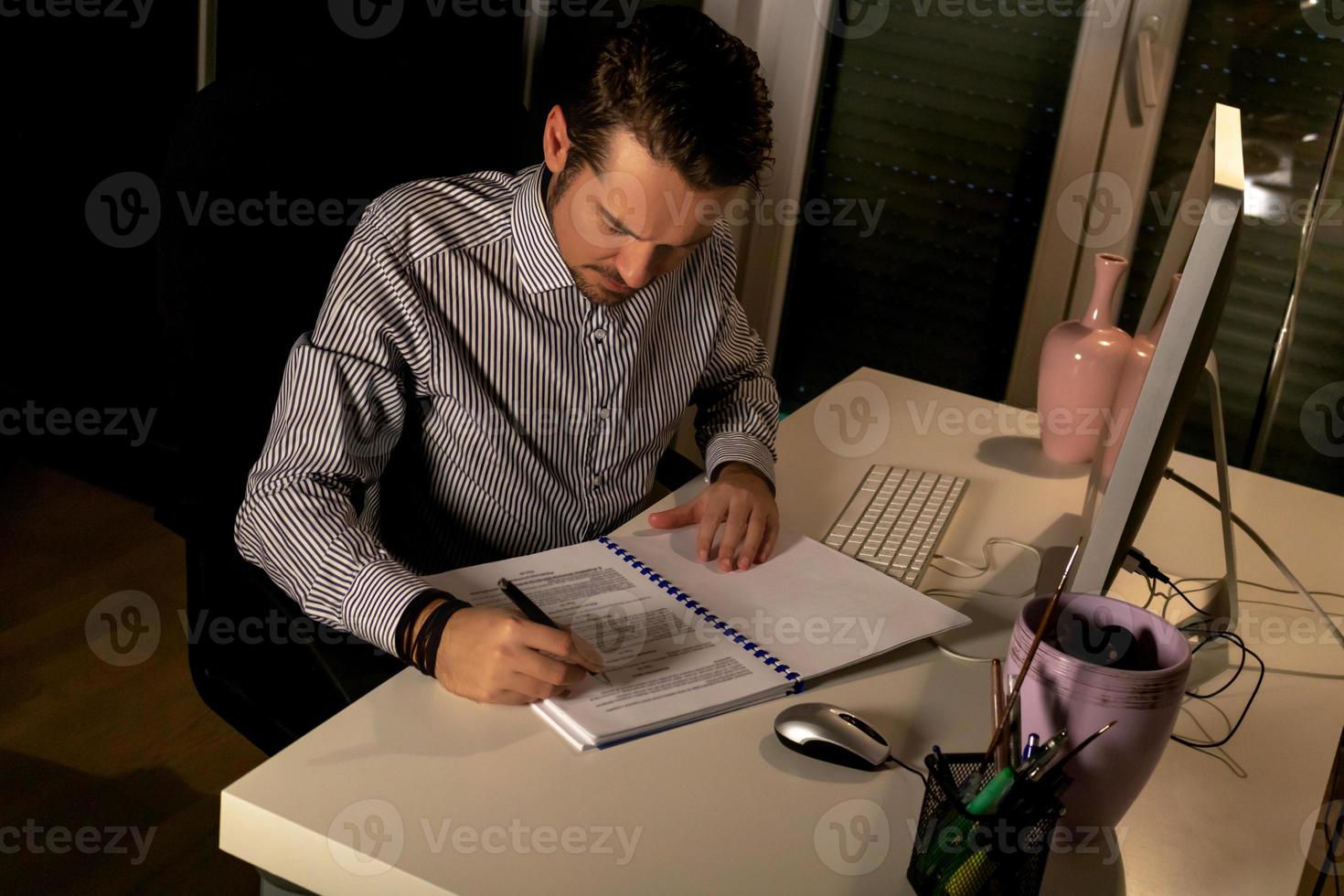 empresário escrevendo relatórios enquanto trabalhava até tarde no escritório. foto