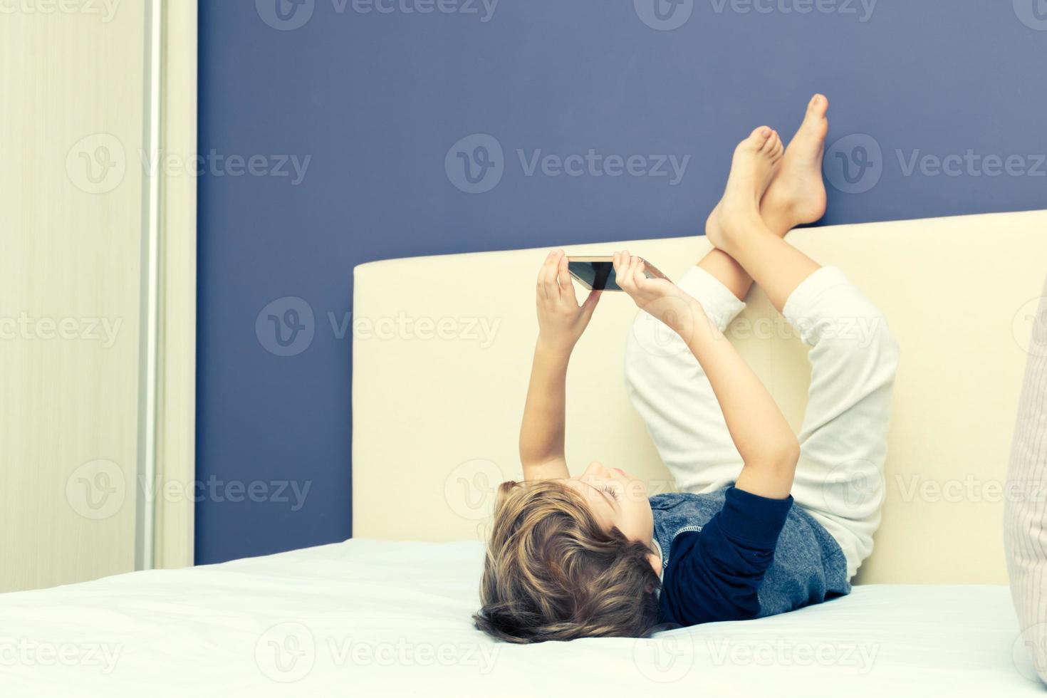 menina bonitinha segurando smartphone olhando para a tela sorrindo usando o  aplicativo, jogando jogos online, assistindo desenhos animados na sala de  estar em casa. crianças e conceito de tecnologia moderna 18819982 Foto