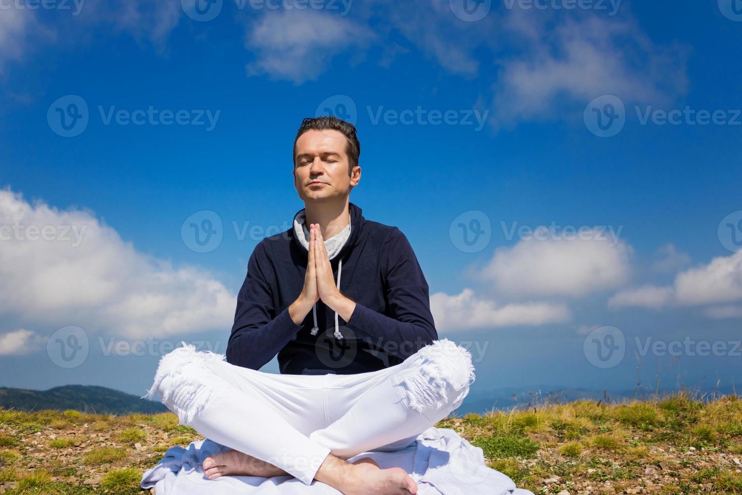 homem calmo em pose de namastê meditando no pico da montanha. foto