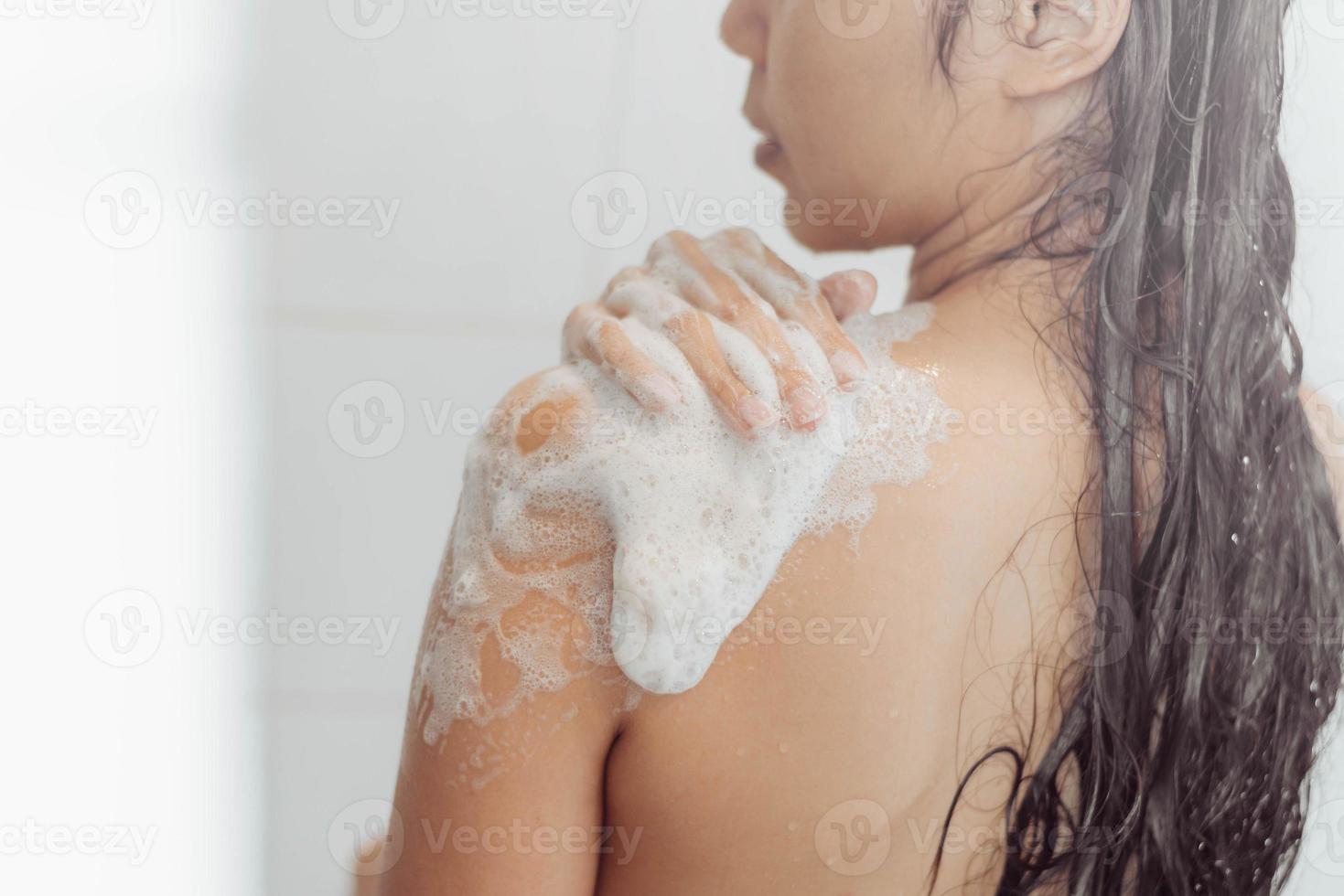 jovem mulher lavando o corpo no chuveiro. mulher asiática tomar banho no banheiro. foto