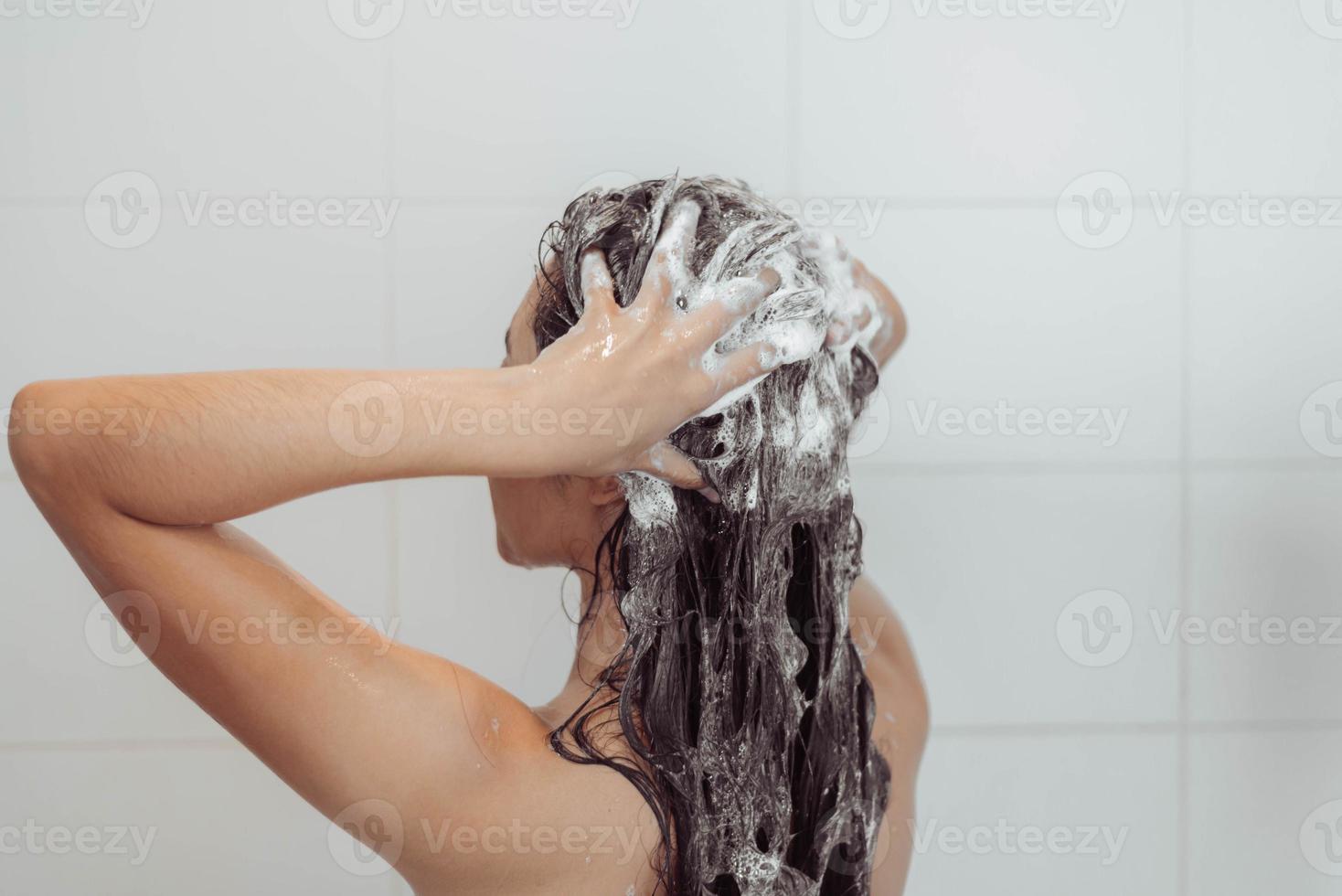 jovem mulher lavando o cabelo no chuveiro. mulher asiática lavando o cabelo preto. foto