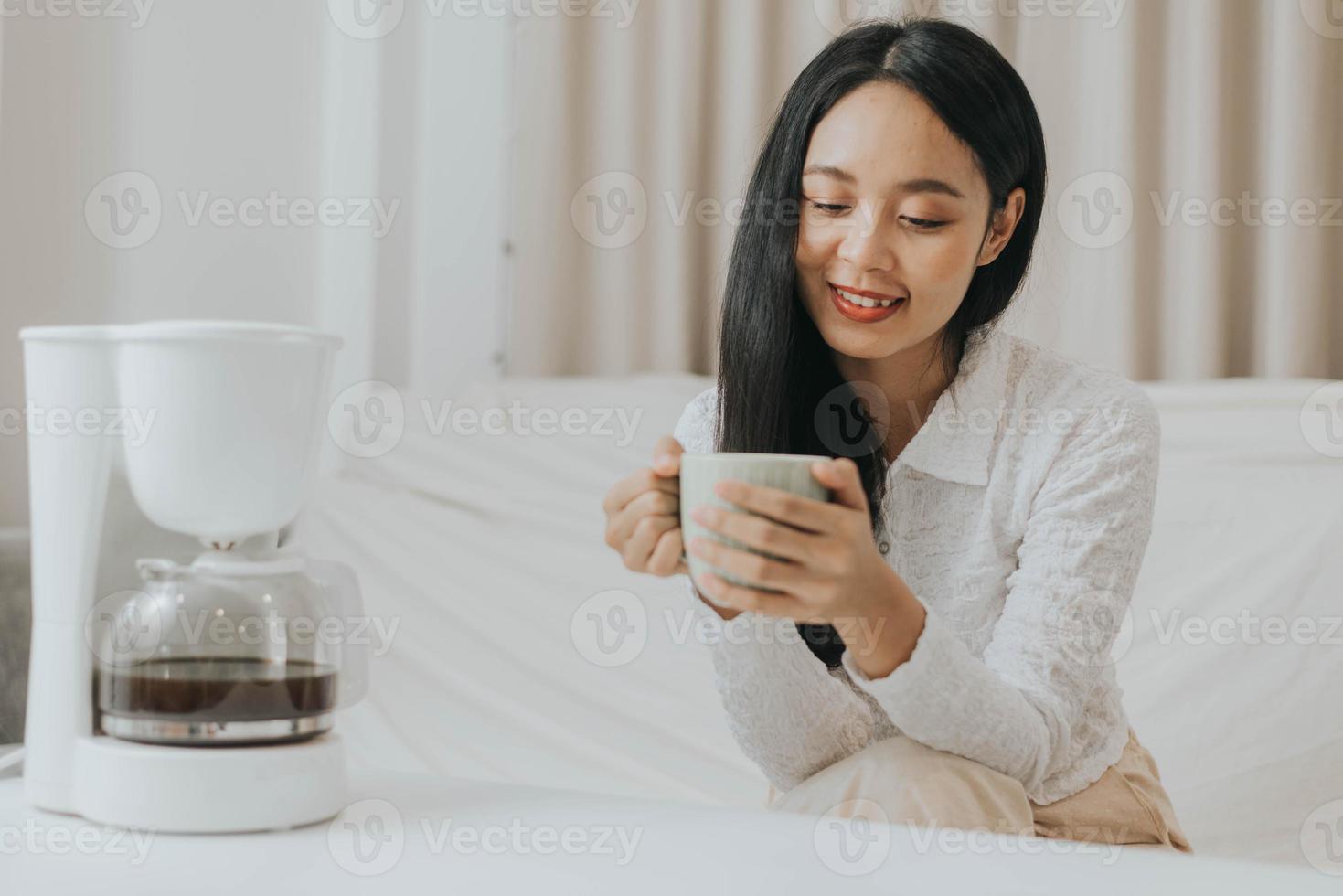 mulher feliz sorrindo e fazendo café em casa. mulher asiática desfrutando e cheirando a café quente da manhã. foto