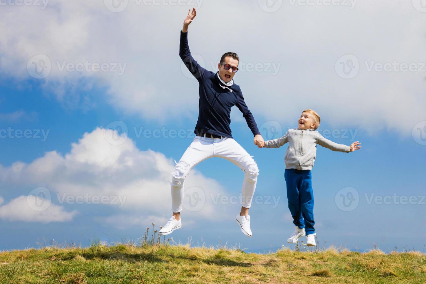 alegre pai e filho de mãos dadas e pulando contra o céu. foto