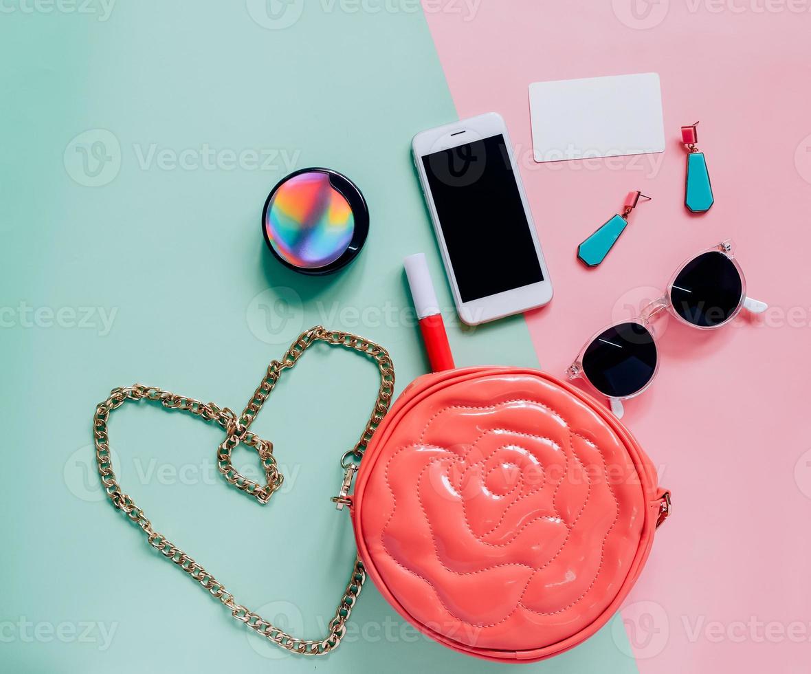 postura plana de bolsa de mulher fofa rosa aberta com cosméticos, acessórios, cartão de etiqueta e smartphone em fundo colorido com espaço de cópia foto