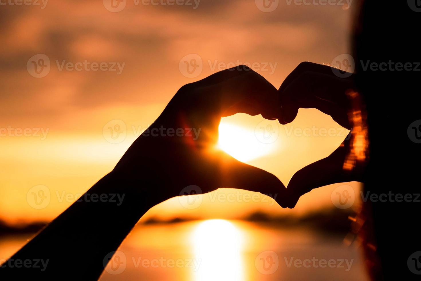 mão de silhueta em forma de coração com nascer do sol no meio e fundo de praia foto
