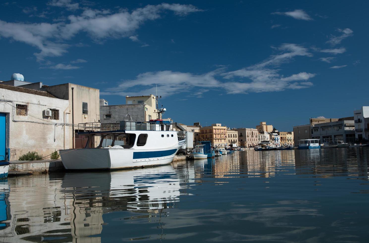 as margens do rio mazaro em mazara del vallo, itália. as casas são refletidas na água. um barco está ancorado na costa. o céu e as nuvens são refletidas nas ondas. foto