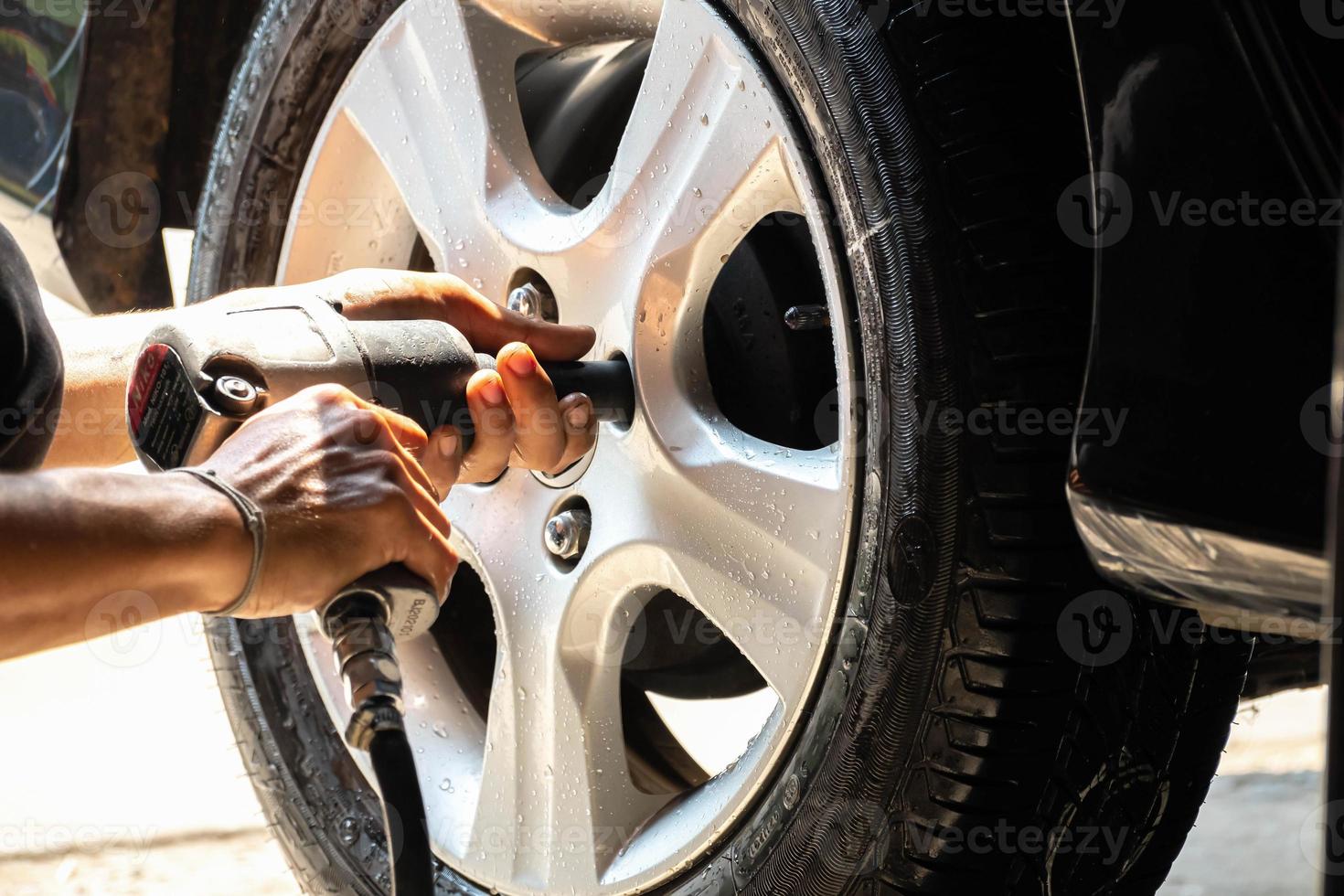 mão de um mecânico de automóveis segurando uma máquina de torneamento de porcas. para desmontar a roda do carro para o corpo do carro durante os reparos foto