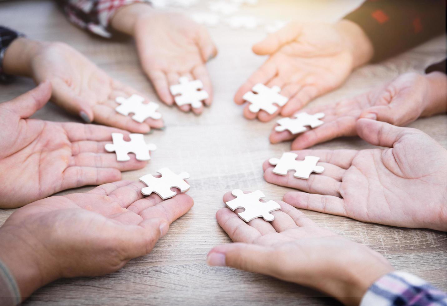 mãos de diversas pessoas montando quebra-cabeças, equipe de jovens junta as peças procurando a combinação certa, ajuda a apoiar o trabalho em equipe para encontrar um conceito de solução comum, vista superior de perto foto