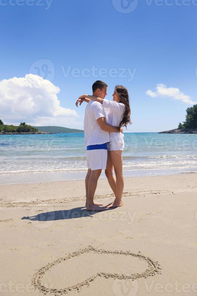 casal feliz se diverte na praia com coração na areia foto