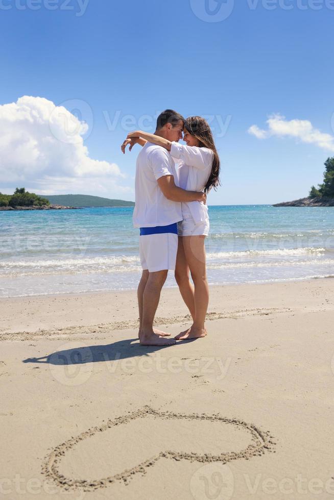 casal feliz se diverte na praia com coração na areia foto