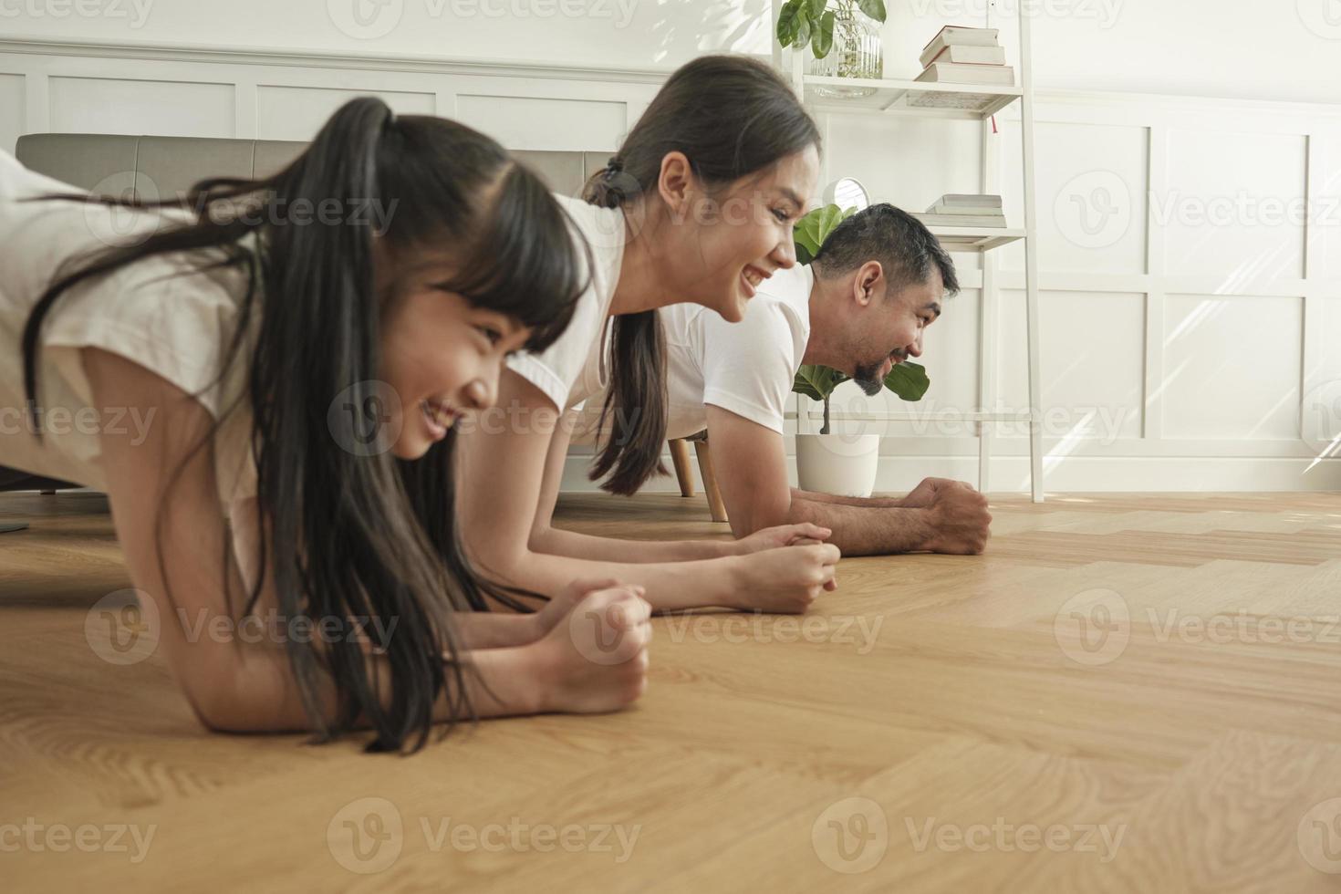 pais tailandeses asiáticos e filha exercício de treinamento de fitness e prática de ioga no chão da sala de estar, adorável remo juntos para saúde e bem-estar e estilo de vida doméstico feliz no fim de semana em família. foto