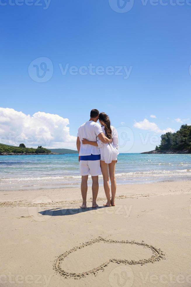 casal romântico apaixonado se diverte na praia com desenho de coração na areia foto