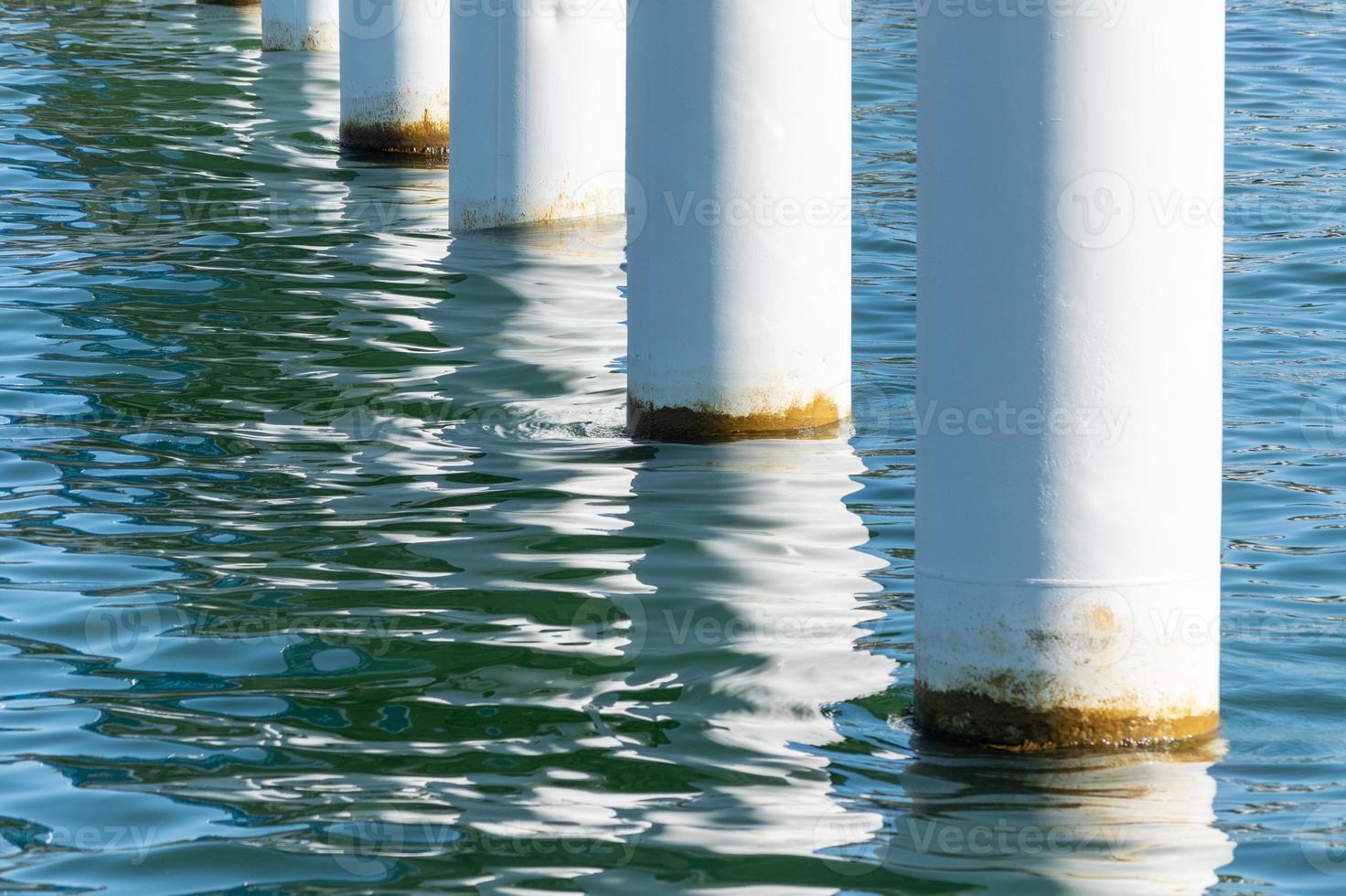 postes de cais enferrujados em água salgada do mar. colunas brancas diagonais. pilares de montagem para ponte. tempo ensolarado. foto