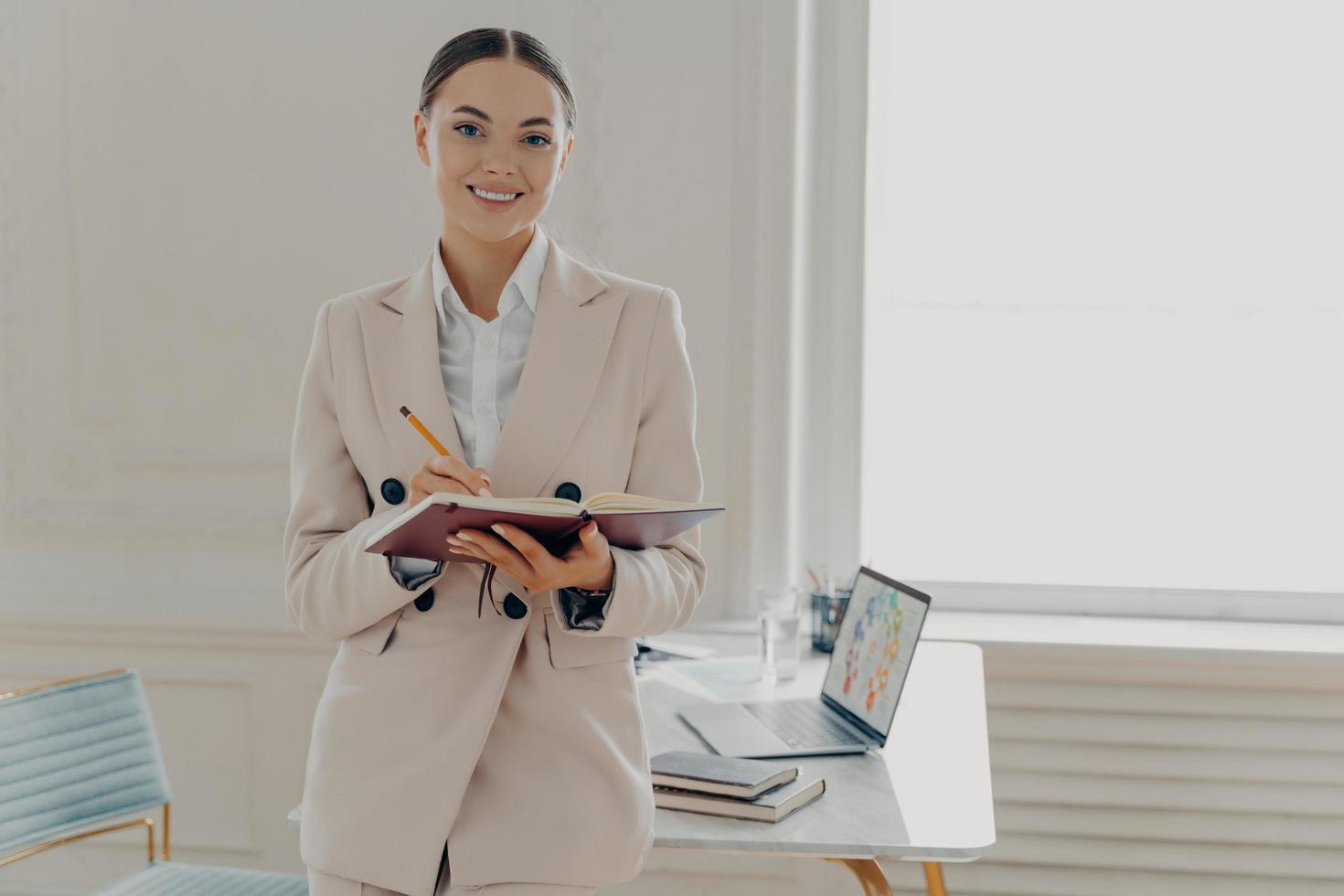 diretora feliz positiva em roupas elegantes, planejando o dia de trabalho enquanto está no escritório foto