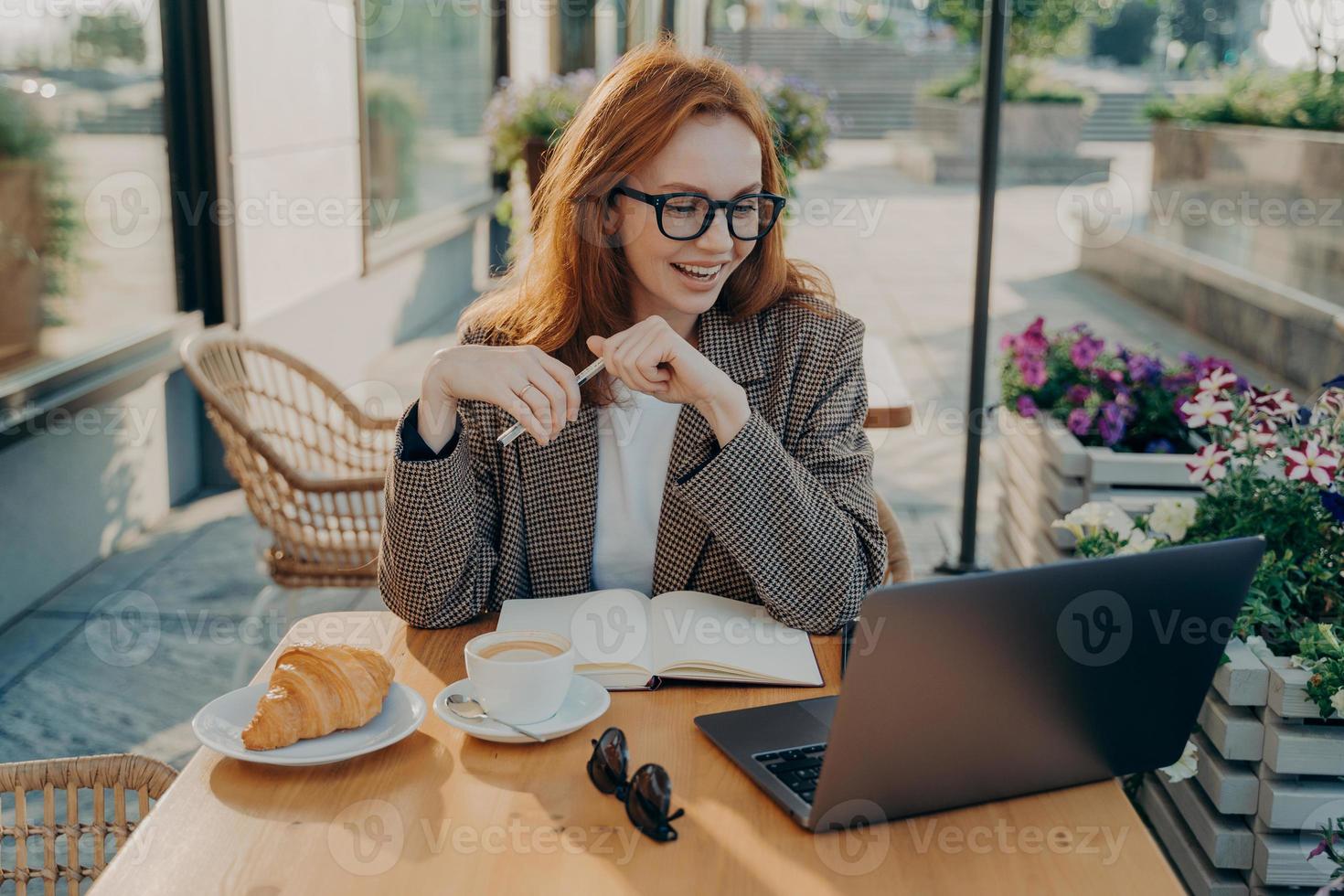 jovem mulher sorridente sentada na mesa de café ao ar livre e assistindo aula online ou webinar no laptop foto
