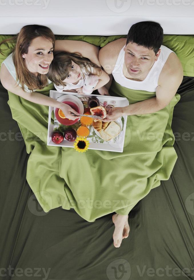 família jovem feliz toma café da manhã na cama foto
