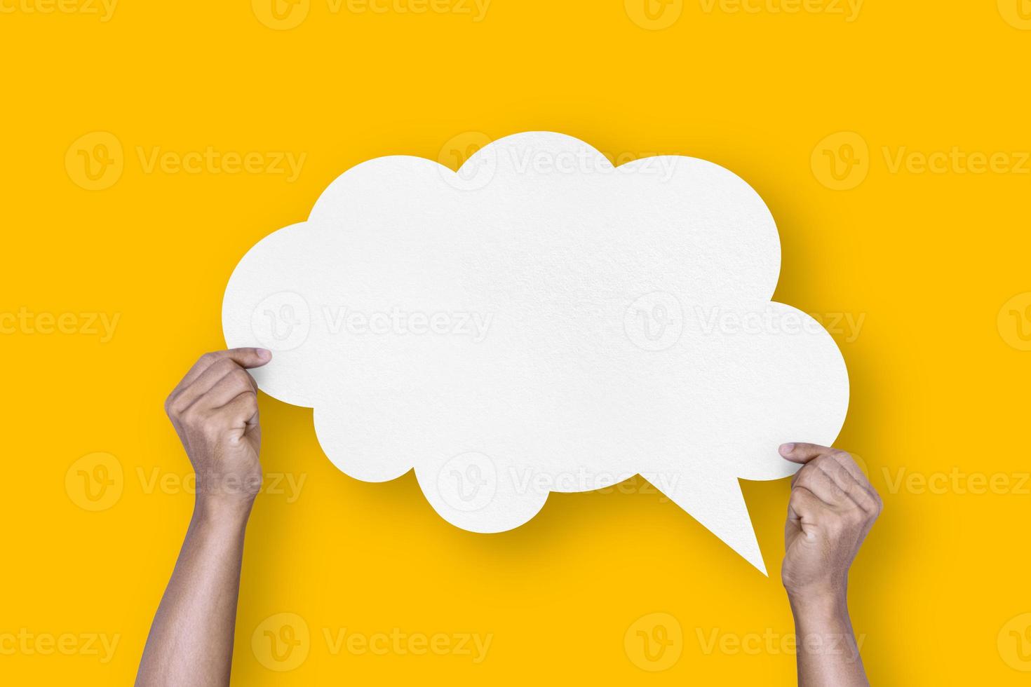 mão segurando o balão de bolha do discurso em forma de nuvem de papel branco isolado em bolhas de comunicação de fundo amarelo foto