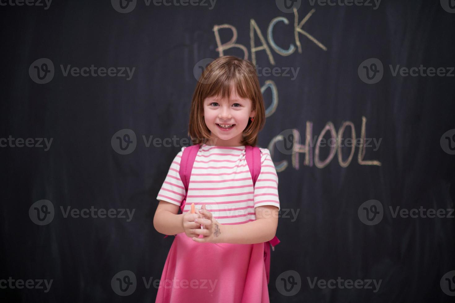 menina da escola com mochila escrevendo lousa foto