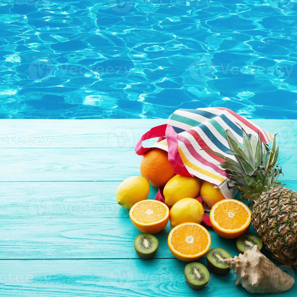 comida fresca cítrica perto da piscina. férias de verão. laranja, kiwi, abacaxi, limão e concha do mar sobre fundo azul de madeira. férias e vista summertime.top e copie o espaço. brincar foto