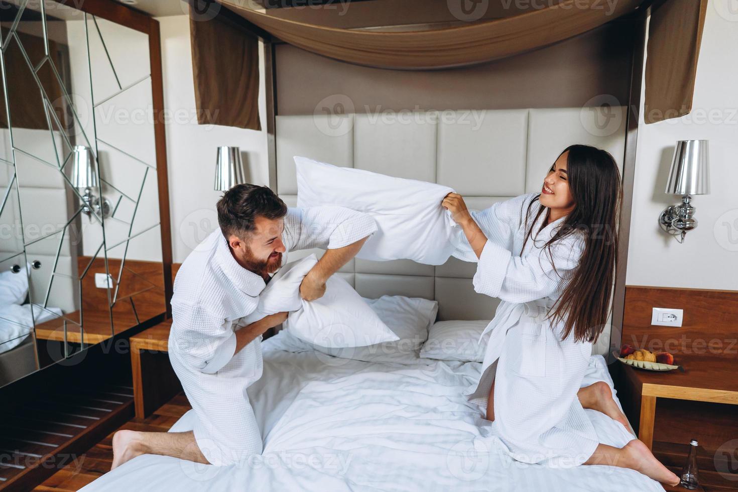 casal alegre se diverte no quarto lutando com grandes almofadas em casa foto