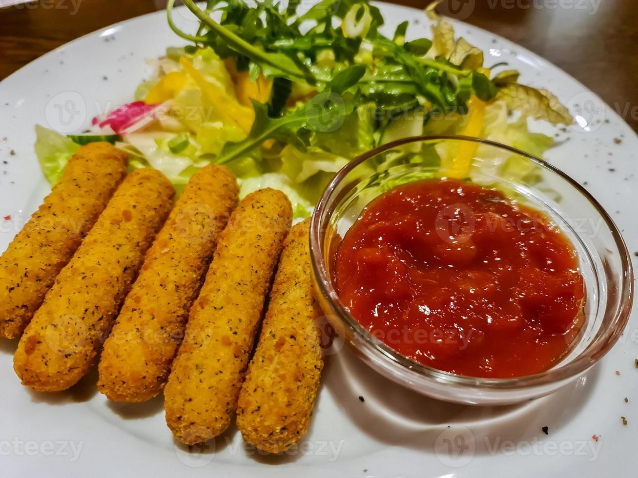 palitos de mussarela, ketchup e salada dispostos em um prato branco. foto