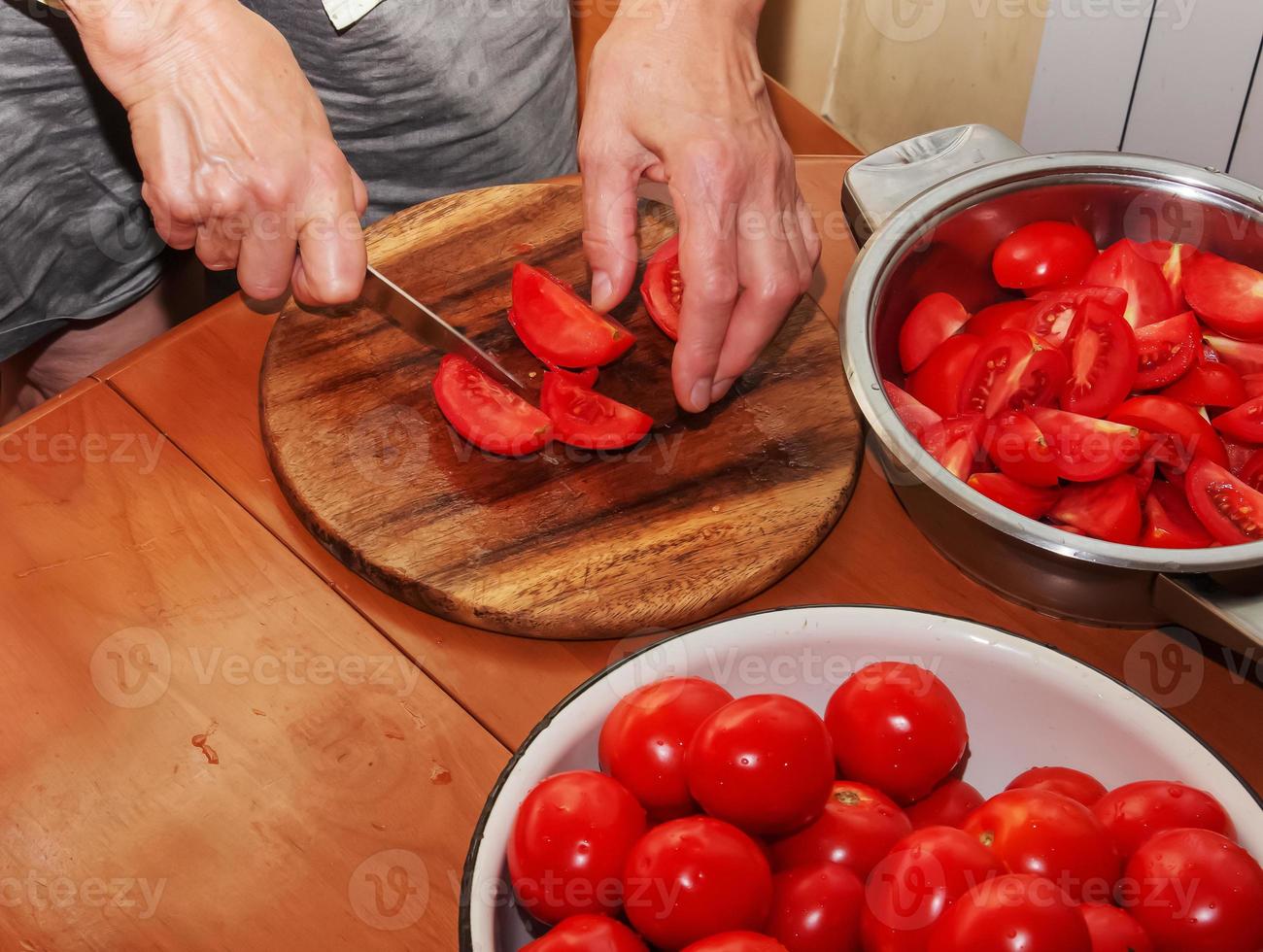 uma mulher prepara suco fresco e saudável de tomate. mãos femininas cortam legumes em uma tábua de cozinha de madeira. conceito de dieta para um estilo de vida saudável. foto