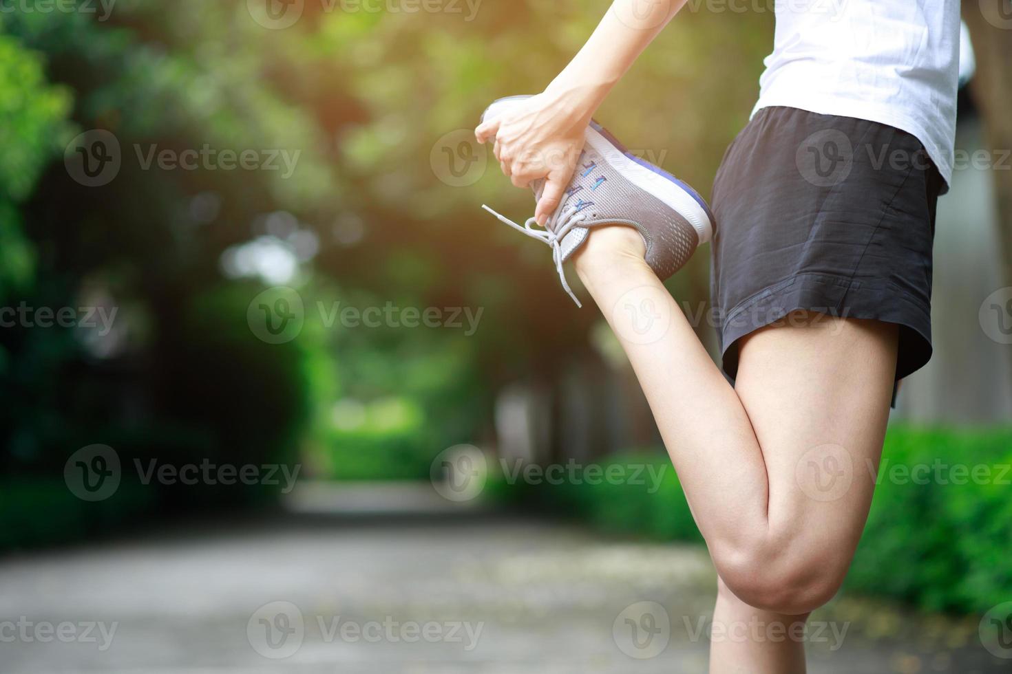 jovem corredora se alongando para se aquecer antes de correr ou malhar no parque. exercício do atleta de atletismo. conceito de estilo de vida saudável de fitness e esporte. foto