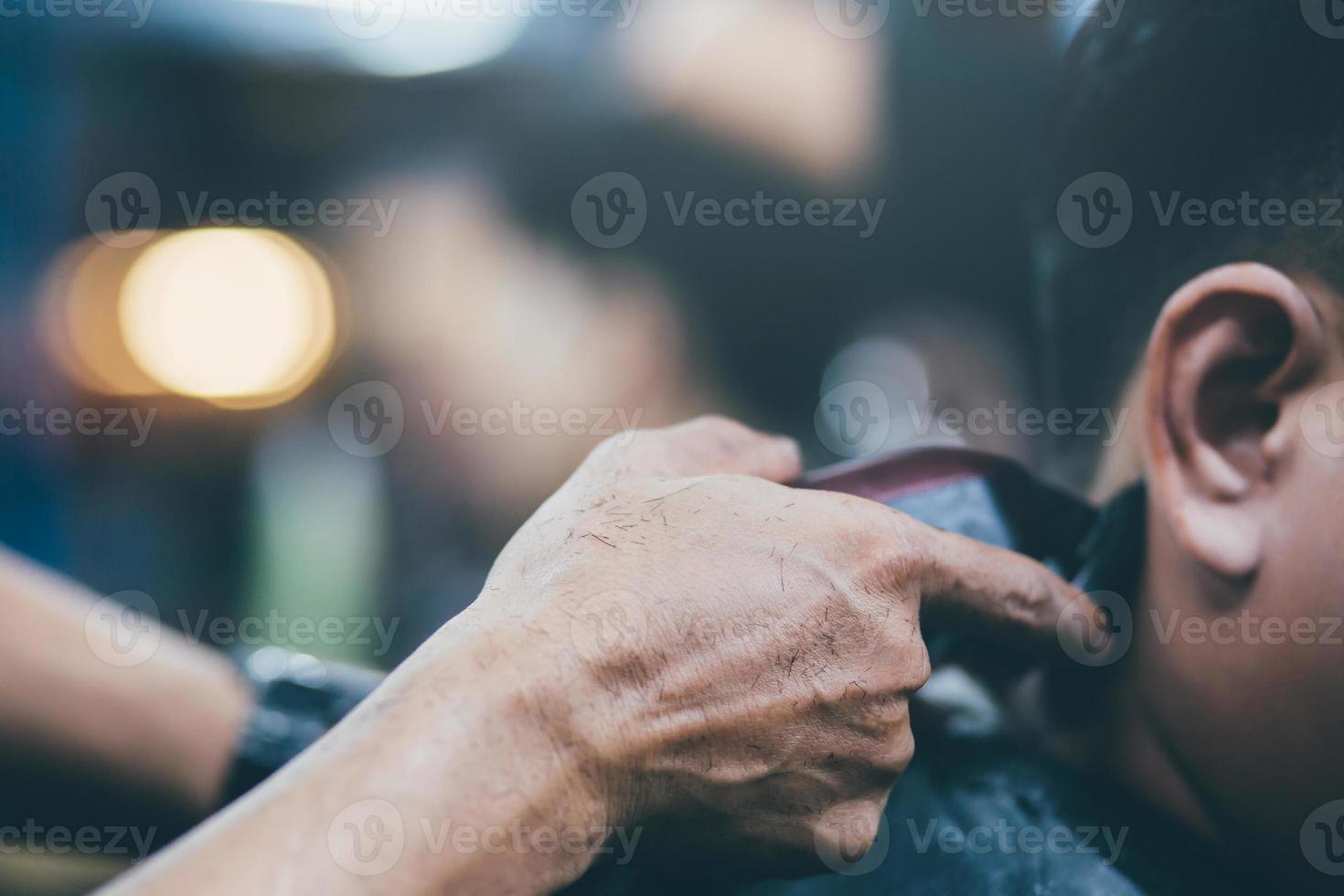 pessoa homem corte de cabelo ficando elegante cabelo vintage barbear, com máquina de cortar cabelo por cabeleireiro barbeiro com as mãos na barbearia. tom vintage de enchimento e foco suave seletivo. foto