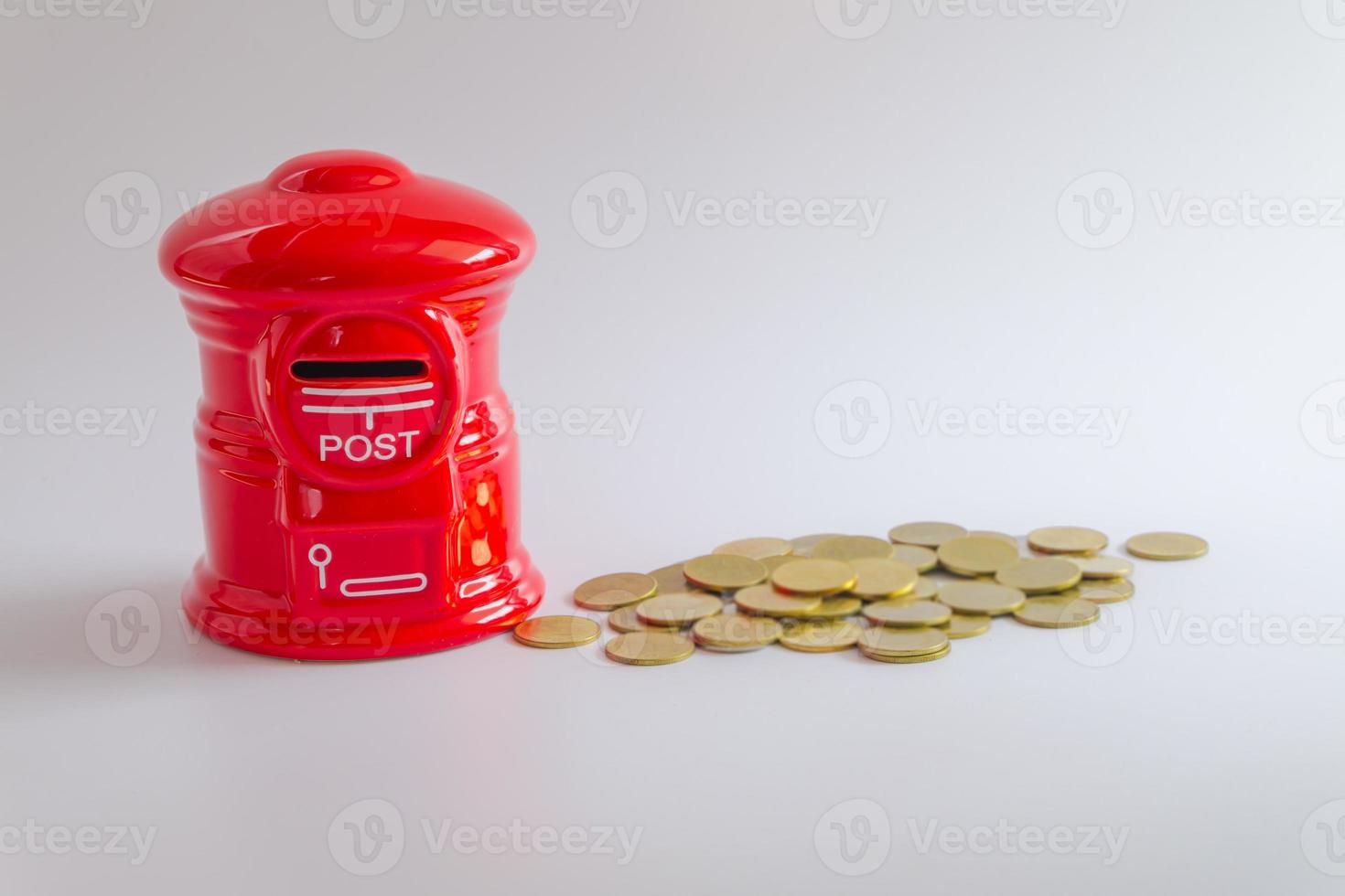 cofrinho ou caixa de dinheiro em forma de caixa de correio vermelha com pilha de moedas de dinheiro crescendo em fundo branco, foco seletivo foto
