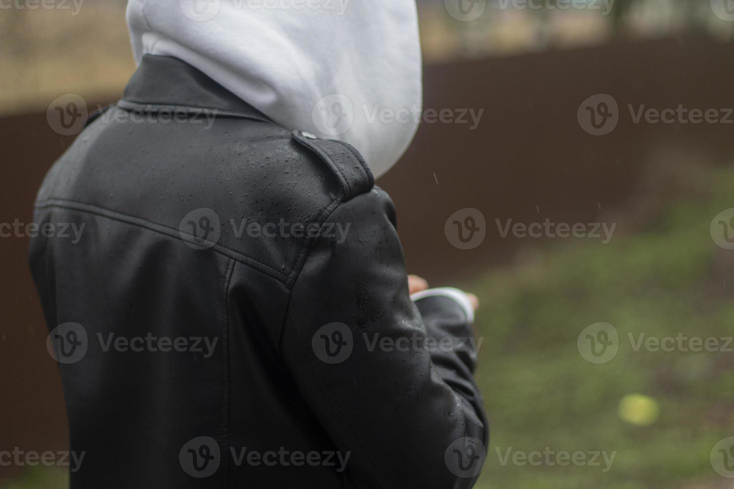 um adolescente anda pela rua com um capuz cinza e uma jaqueta de couro preta, vista lateral. roupas casuais, vistas de outono. foto