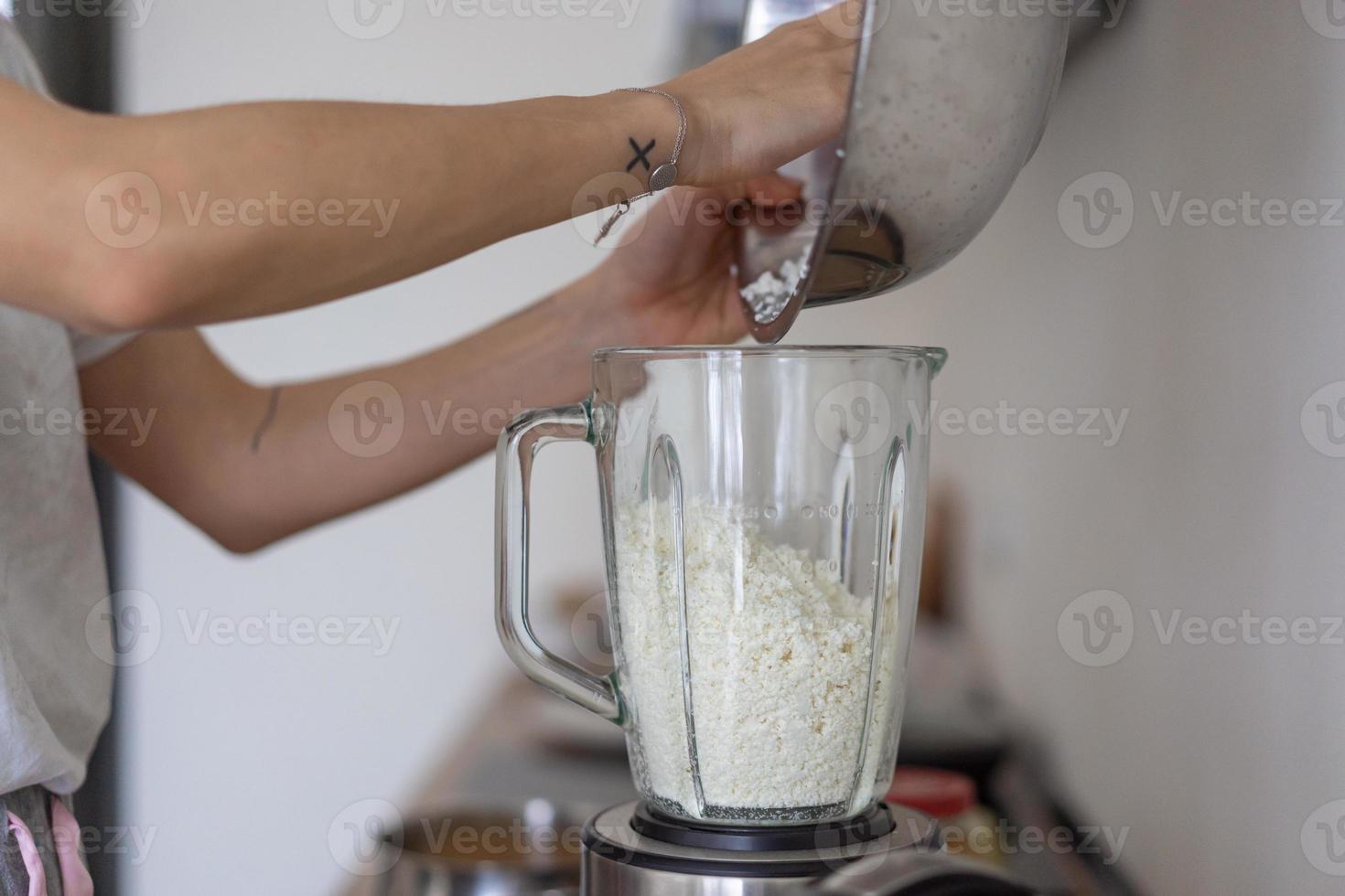 mulher derramando queijo cottage em um liquidificador na cozinha foto
