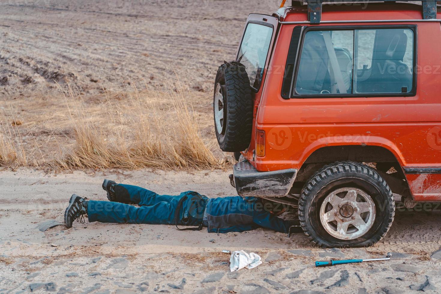 homem encontra-se sob um carro 4x4 em uma estrada de terra foto