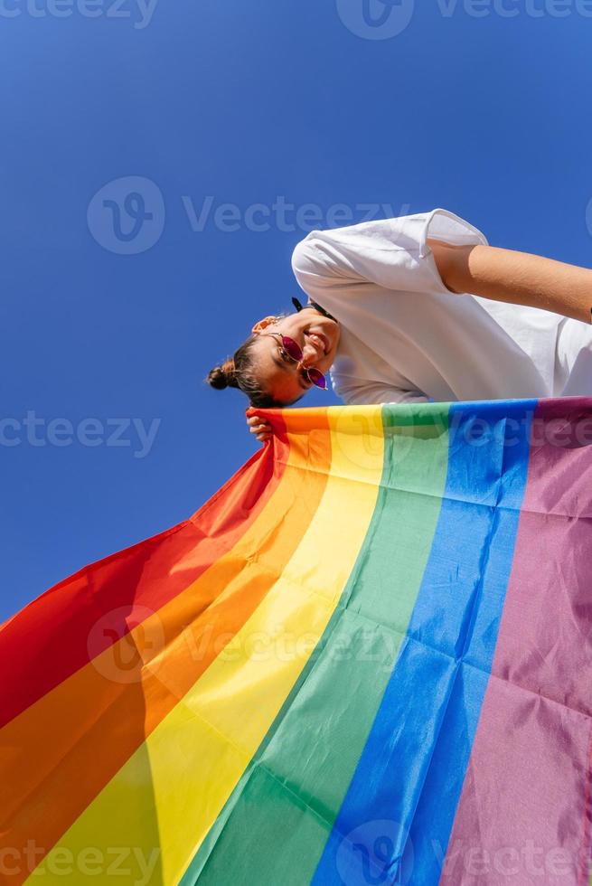 uma jovem desenvolve uma bandeira de arco-íris contra o céu foto