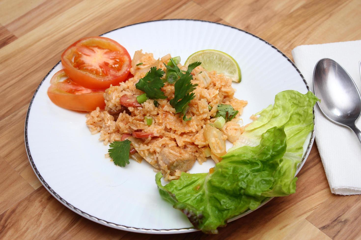 arroz frito de carne de porco e salsicha com cebola servido em um prato branco sobre uma mesa de madeira clara. foto