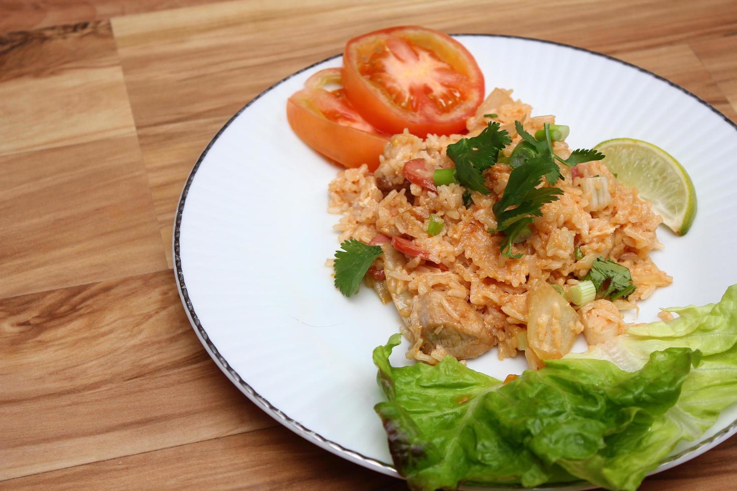 arroz frito de carne de porco e salsicha com cebola servido em um prato branco sobre uma mesa de madeira clara. foto