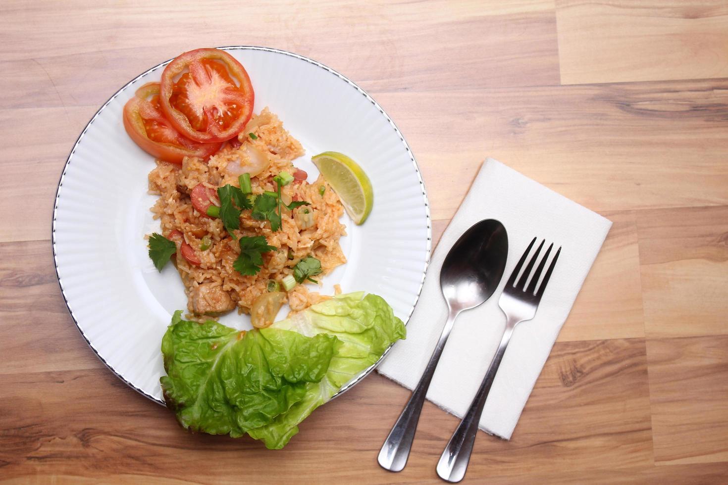 arroz frito de carne de porco e salsicha com cebola servido em um prato branco sobre uma mesa de madeira clara. foto