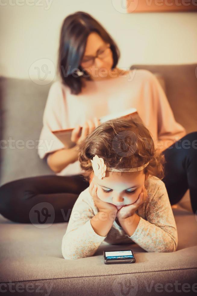 menina usando telefone inteligente enquanto relaxa no sofá com a mãe. foto