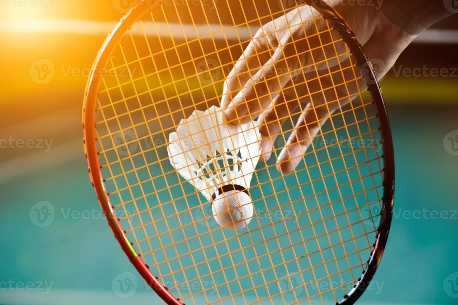 raquete de badminton e peteca branca velha segurando nas mãos do jogador enquanto servia pela rede à frente, desfocar o fundo da quadra de badminton e foco seletivo foto