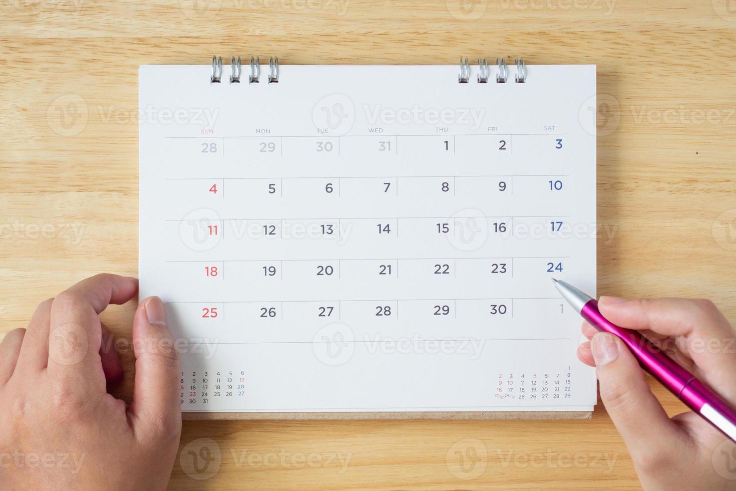 página do calendário na mesa com a mão feminina segurando a caneta, vista superior foto