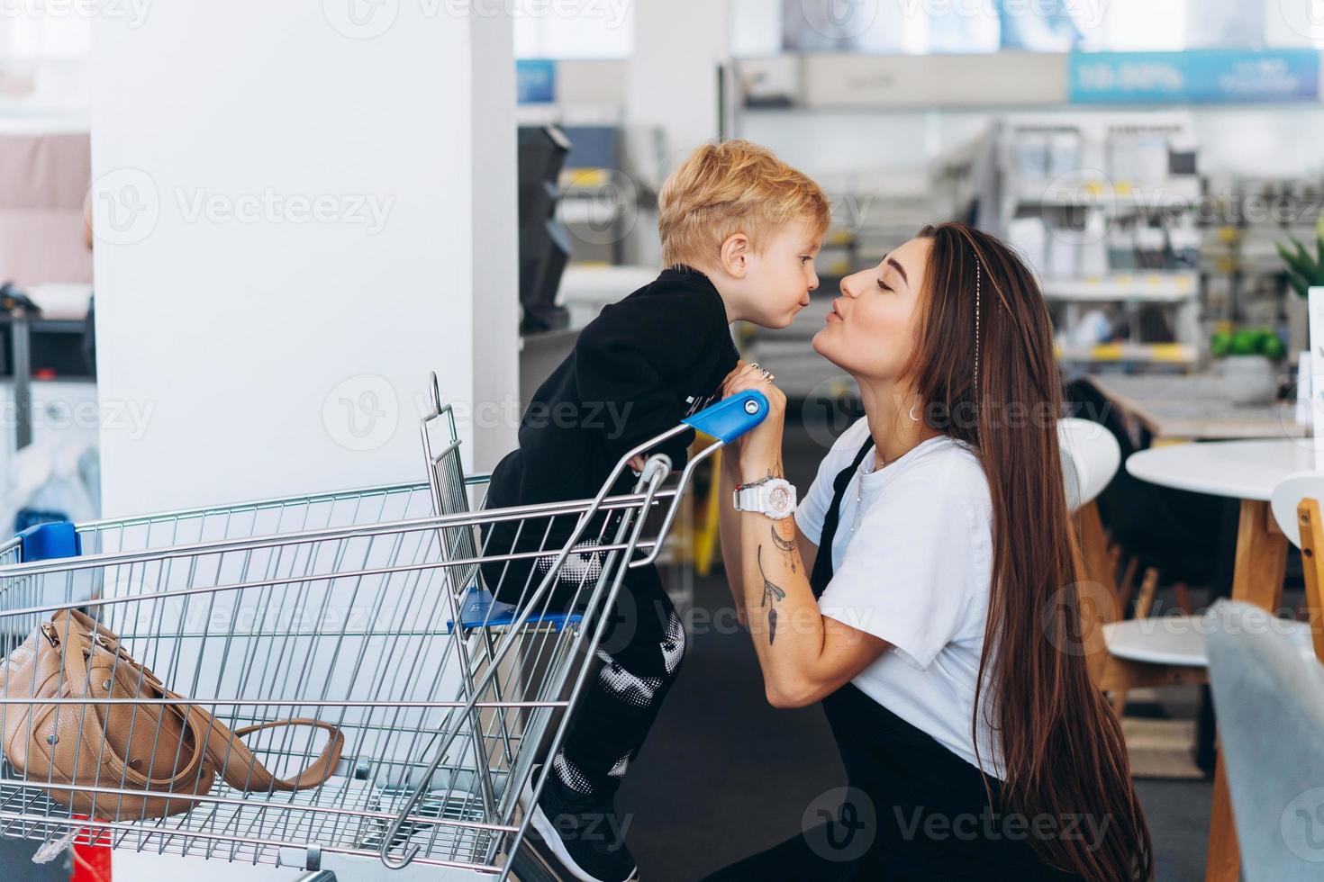 linda mãe carrega seu filho pequeno no carrinho de supermercado foto