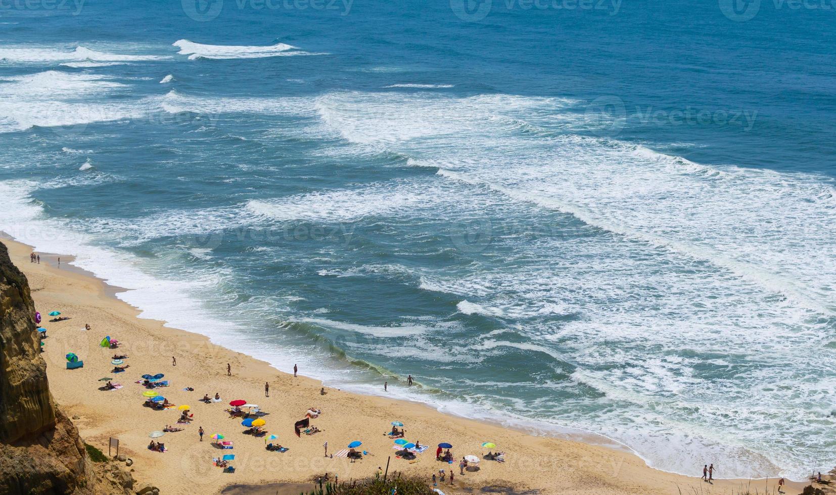 praia à beira-mar com pessoas descansando, local de férias. montanhas, mar e ondas. viajar para a europa portugal. foto