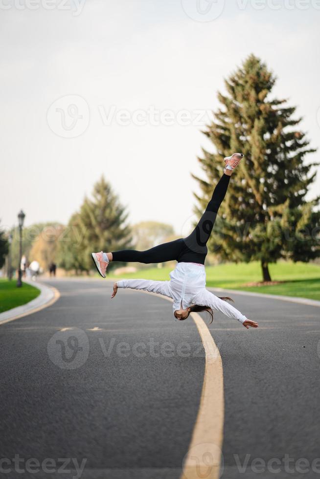 mulher atleta pulando cambalhota na estrada, fazendo exercícios ao ar livre. foto