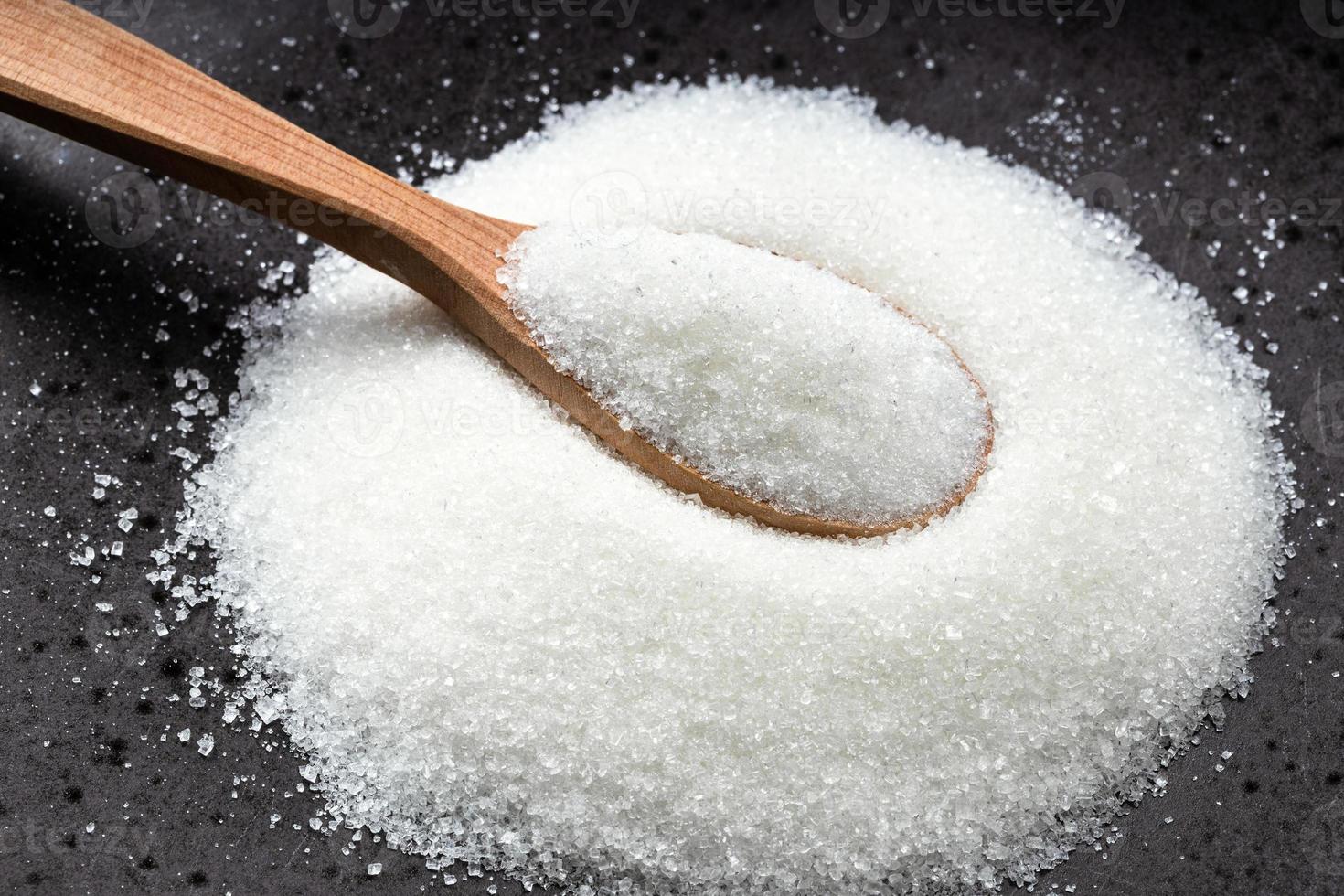 colher de pau com açúcar refinado branco no preto foto