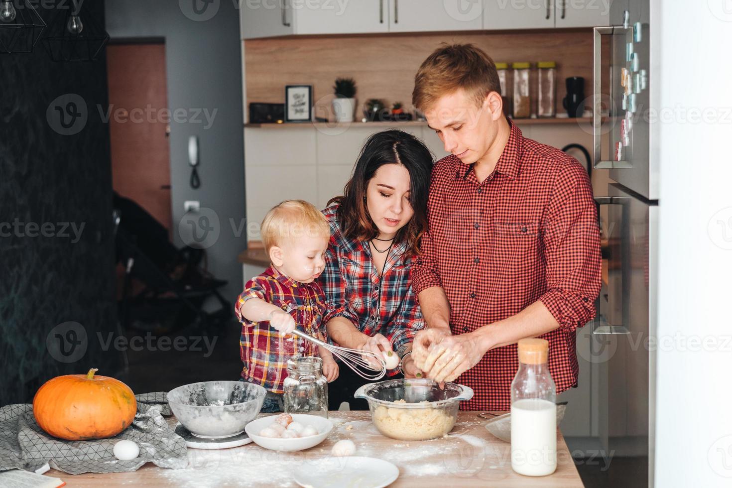 pai, mãe e filho pequeno cozinham uma torta foto