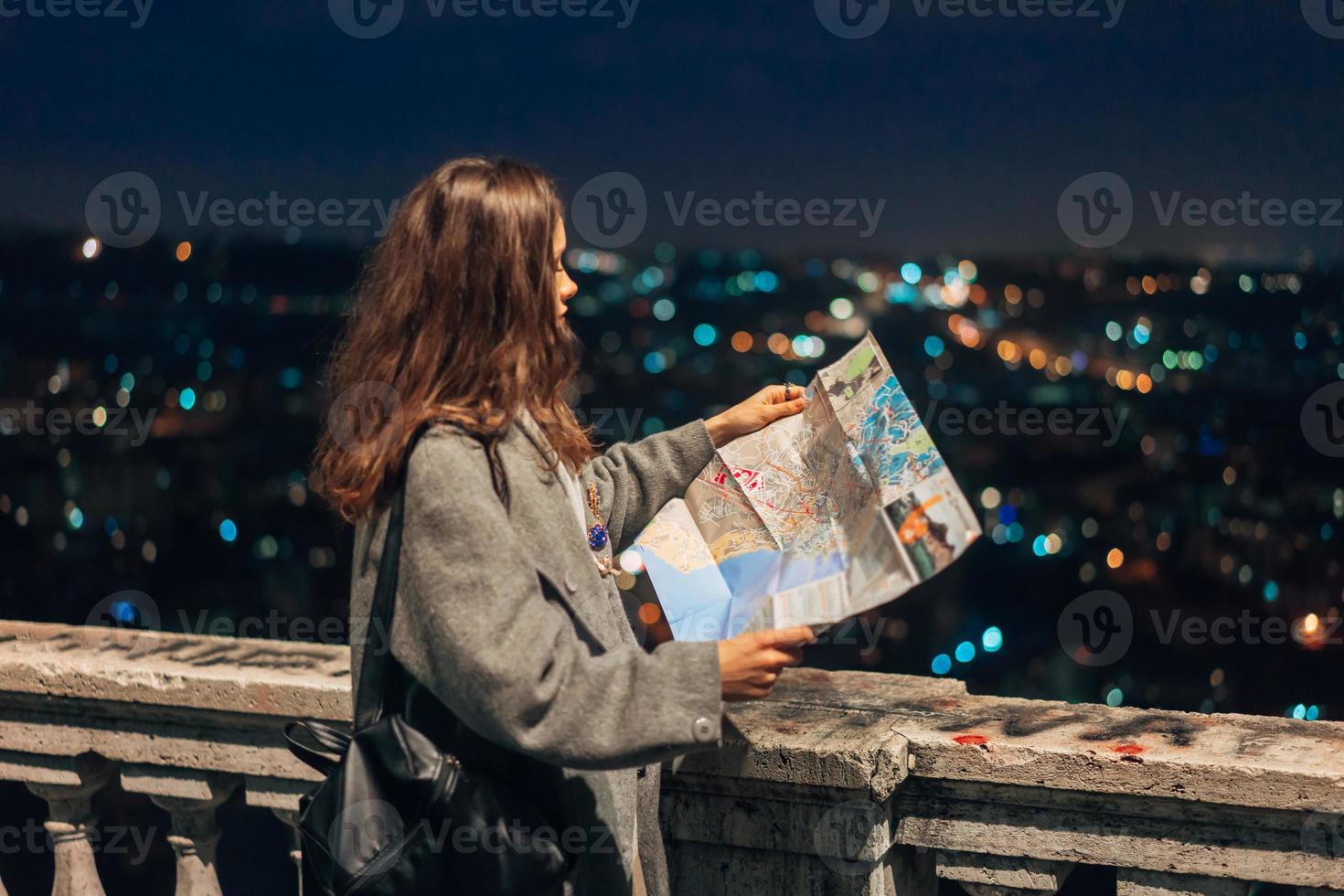 menina com um mapa no fundo da cidade à noite foto