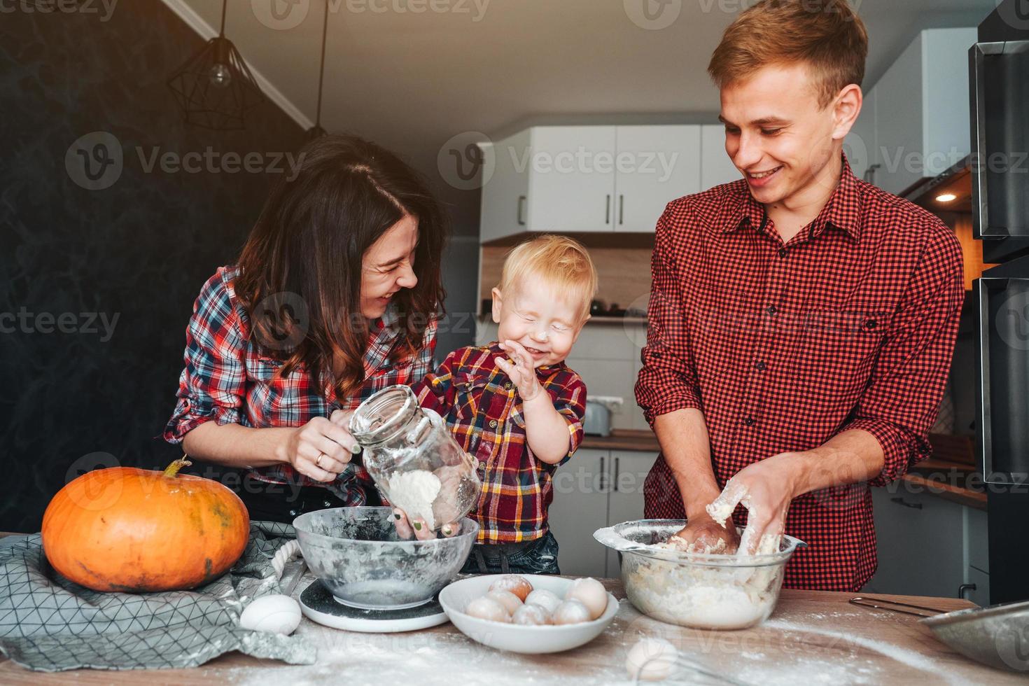 pai, mãe e filho pequeno cozinham uma torta foto