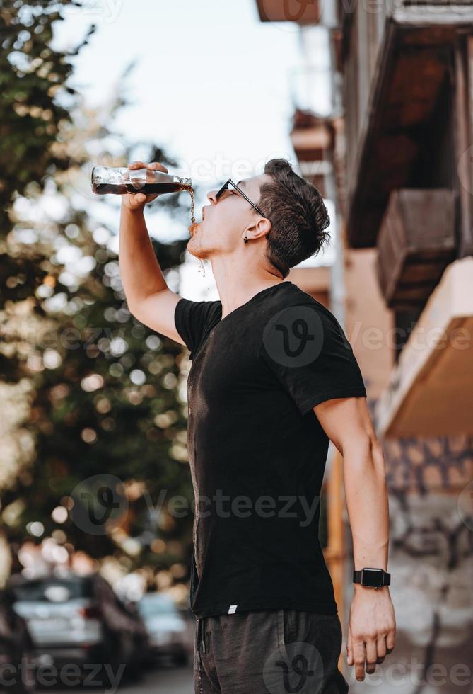 homem jovem hipster atraente na rua bebe uma bebida fresca em um dia de verão. foto