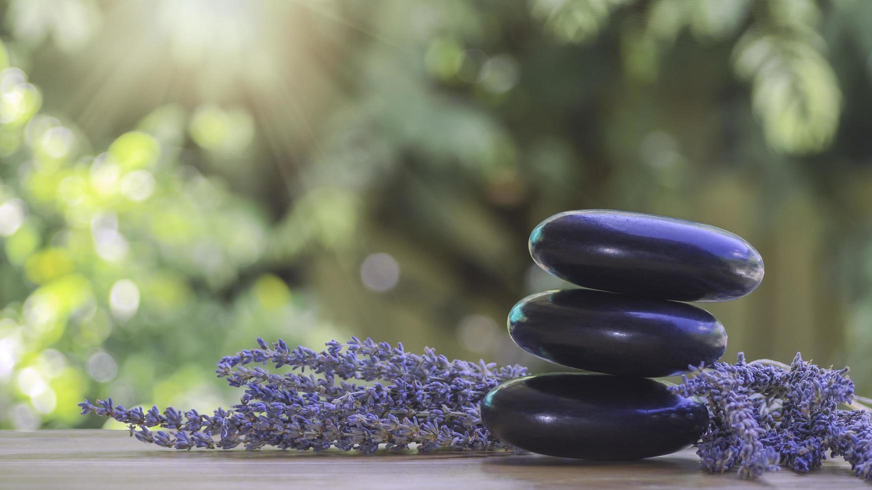 equilíbrio e bem-estar ou conceito de saúde com pilha de pedras de spa pretas em madeira e picos de floração de lavanda com aromaterapia. a vista lateral e a composição da paisagem parecem relaxadas. foto