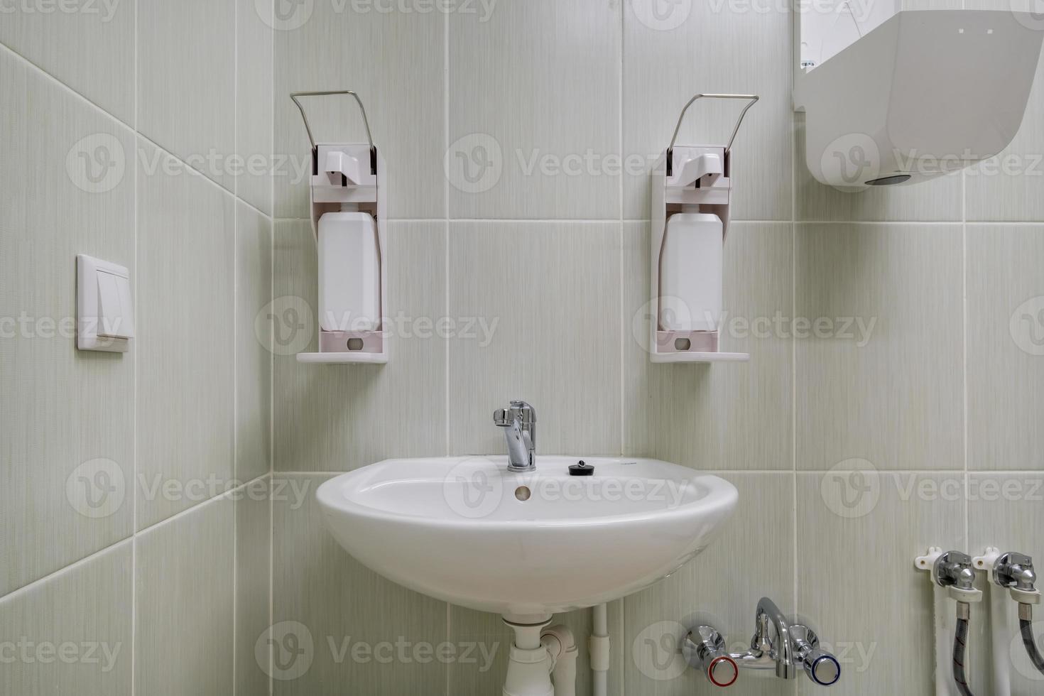 sabonete de cotovelo e dispensador anti-séptico ou desinfetante montado na parede para desinfecção das mãos e pia de torneira de água com torneira banheiro ou clínica foto